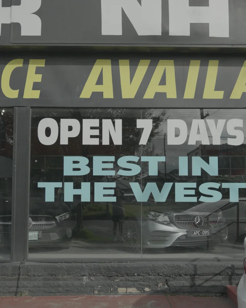 Car dealership showroom window with cut vinyl lettering reading Open 7 Days, Best in the West